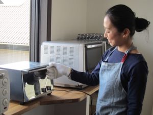 ドデカパン（フォカッチャ）焼き上がり直前。トースターはパン生地を焼くので、火加減が調整できて天板が広いものを愛用。エプロンはあざみ野のグランジャポンで購入した作家さんの作品。手に付けているのはなんと軍手！　アツアツの焼きたてパンやオーブンを触るには、軍手が最高！　だそうです。なぜなら指が5本使えるから。1枚では熱いので、2枚重ね